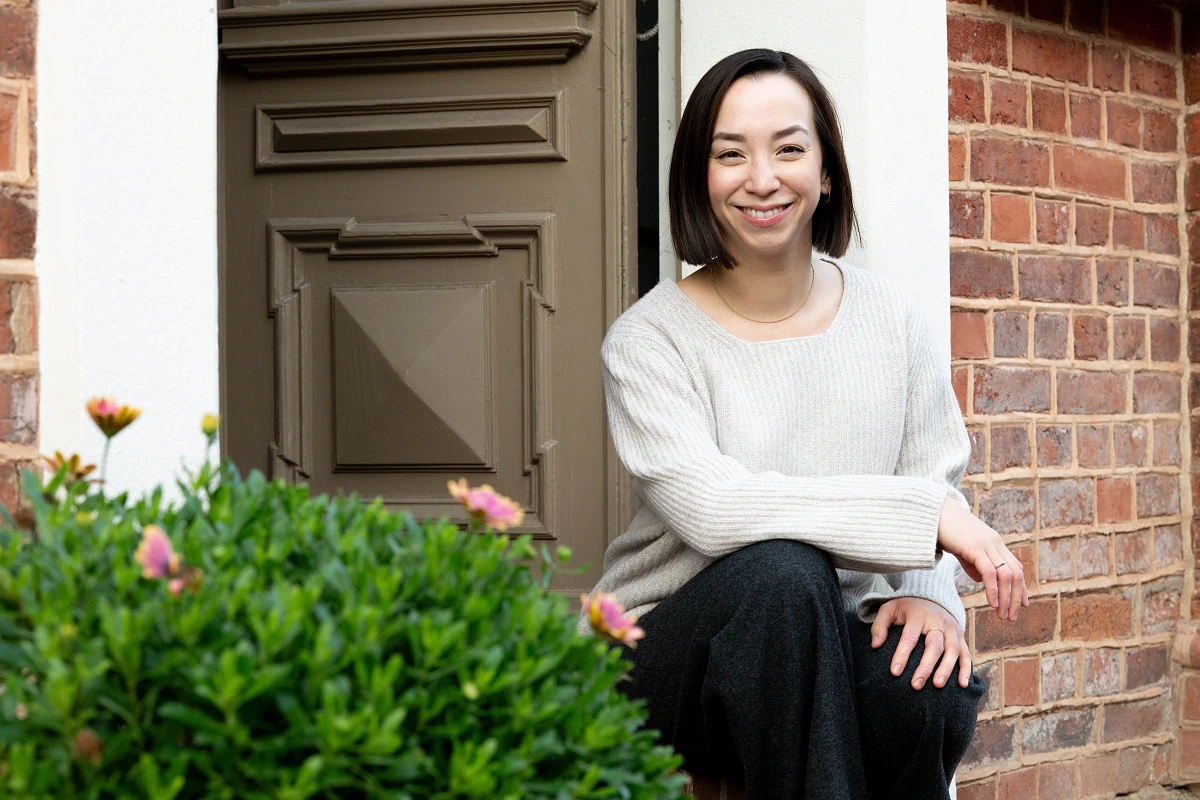 Firmenportrait Arztpraxis Aerztin Vor Praxis Eingang Sitzend Mit Schoener Hecke