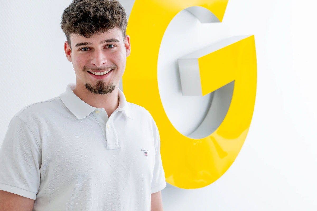 Mitarbeiterportrait Junger Mann Vor Gelbem Firmenlogo